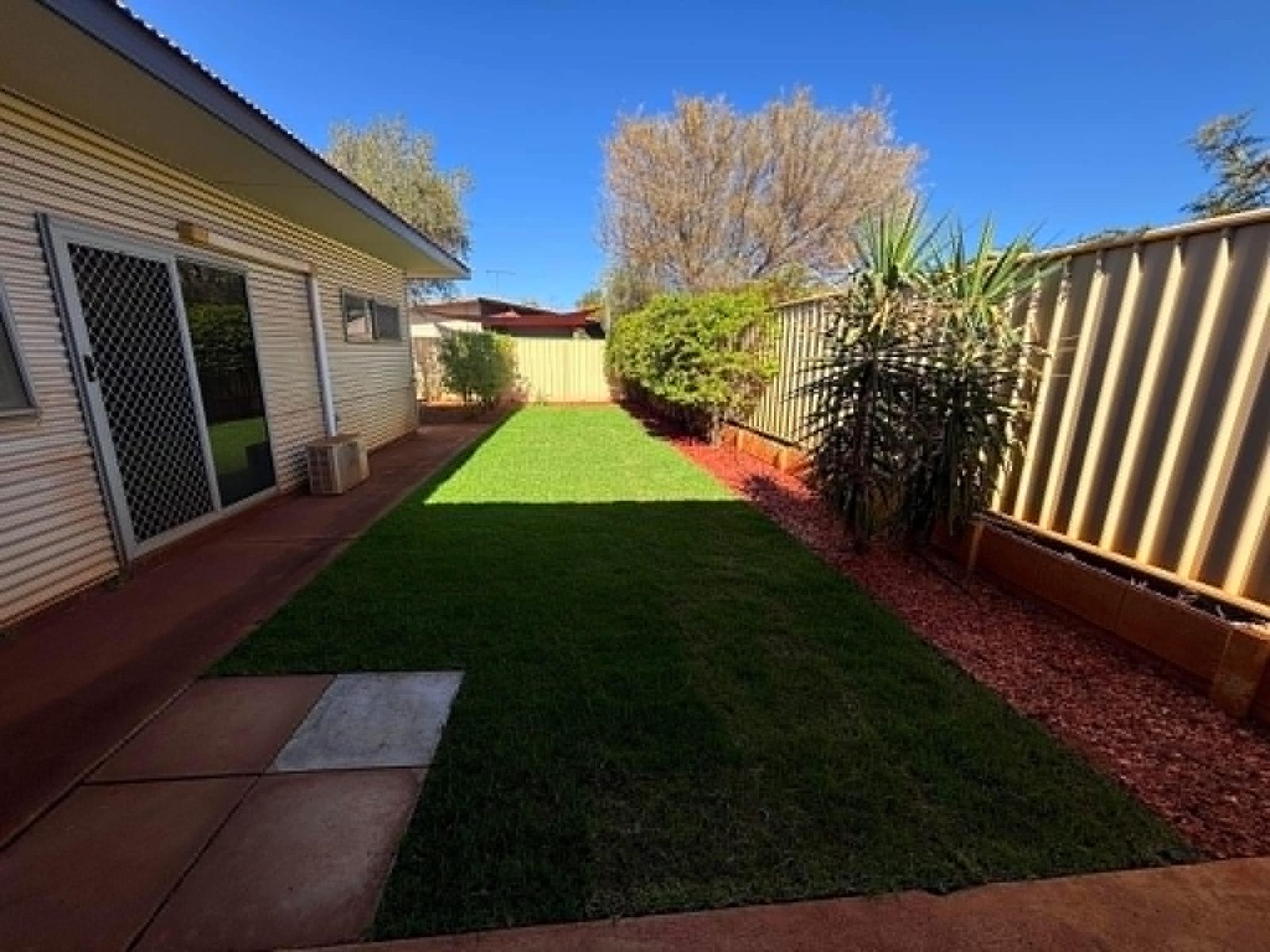 The same backyard with fresh green lawn and garden bed edging after landscaping